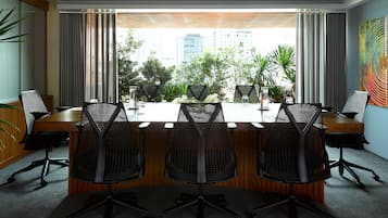 A conference room with a long table, four chairs, and a view of a cityscape through large windows.