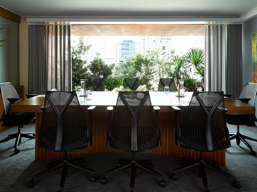 Un salón de conferencias con una larga mesa, cuatro sillas y vistas a un paisaje urbano a través de amplias ventanas.