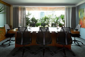 A conference room with a long table, four chairs, and a view of a cityscape through large windows.