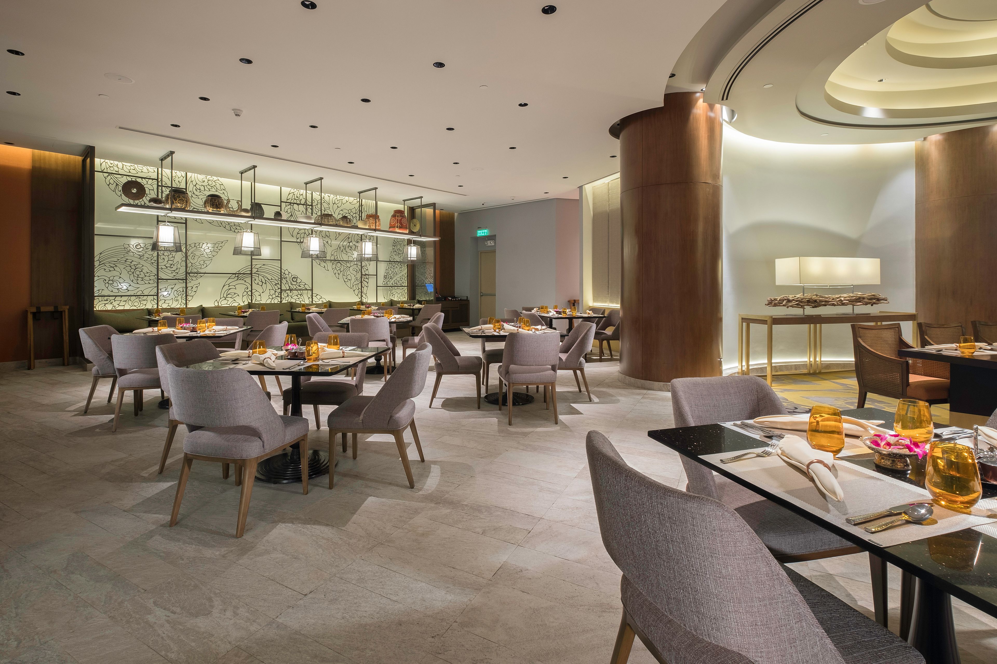 A modern dining area with multiple tables and chairs, a decorative wall with patterns, and a large column.