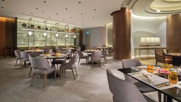 A modern dining area with multiple tables and chairs, a decorative wall with patterns, and a large column.