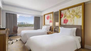 A hotel room with two beds, a desk, a chair, and a large window with a city view.