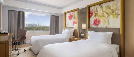A hotel room with two beds, a desk, a chair, and a large window with a city view.