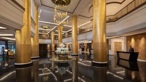 A spacious lobby with high ceilings, large golden columns, a central chandelier, and a reception desk. - Dusit Thani Manila (Makati)