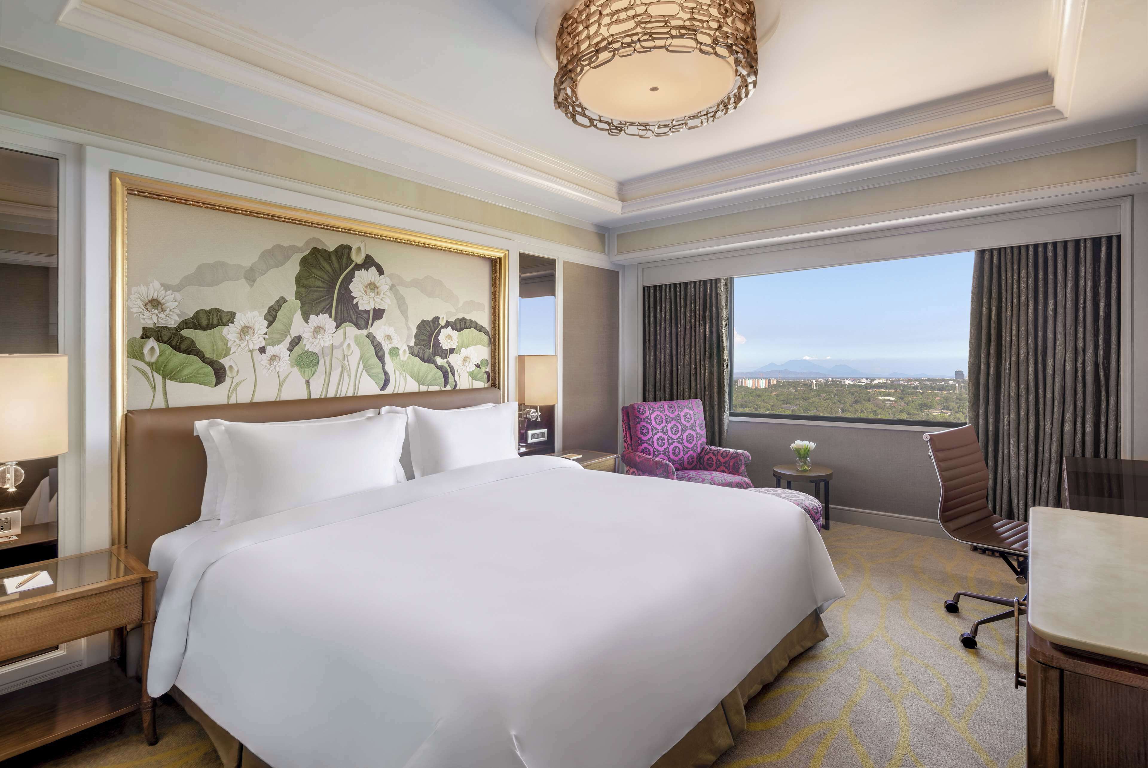 Quarto de hotel com uma cama grande, uma cadeira, uma escrivaninha e vista para a cidade.