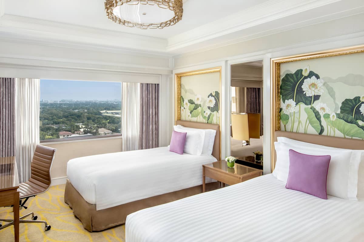 Habitación de hotel con dos camas, un escritorio, una silla, un espejo y vistas a la ciudad.