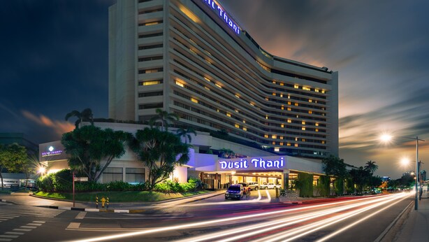 A modern hotel with a curved facade, illuminated signage, and a well-maintained entrance area. - Dusit Thani Manila (Makati)