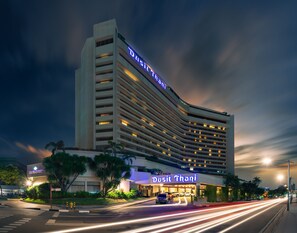 Un hotel moderno con fachada curva, señalización iluminada y un área de entrada bien cuidada.