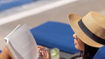 A person reclining on a lounge chair by a pool, reading a book.
