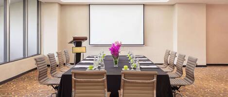 A conference room with a large table, chairs, a projector screen, and a podium.