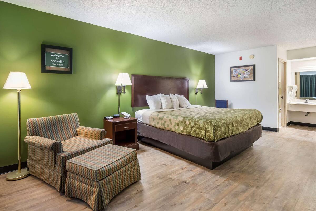 A hotel room with a bed, a chair, a nightstand, and a lamp.