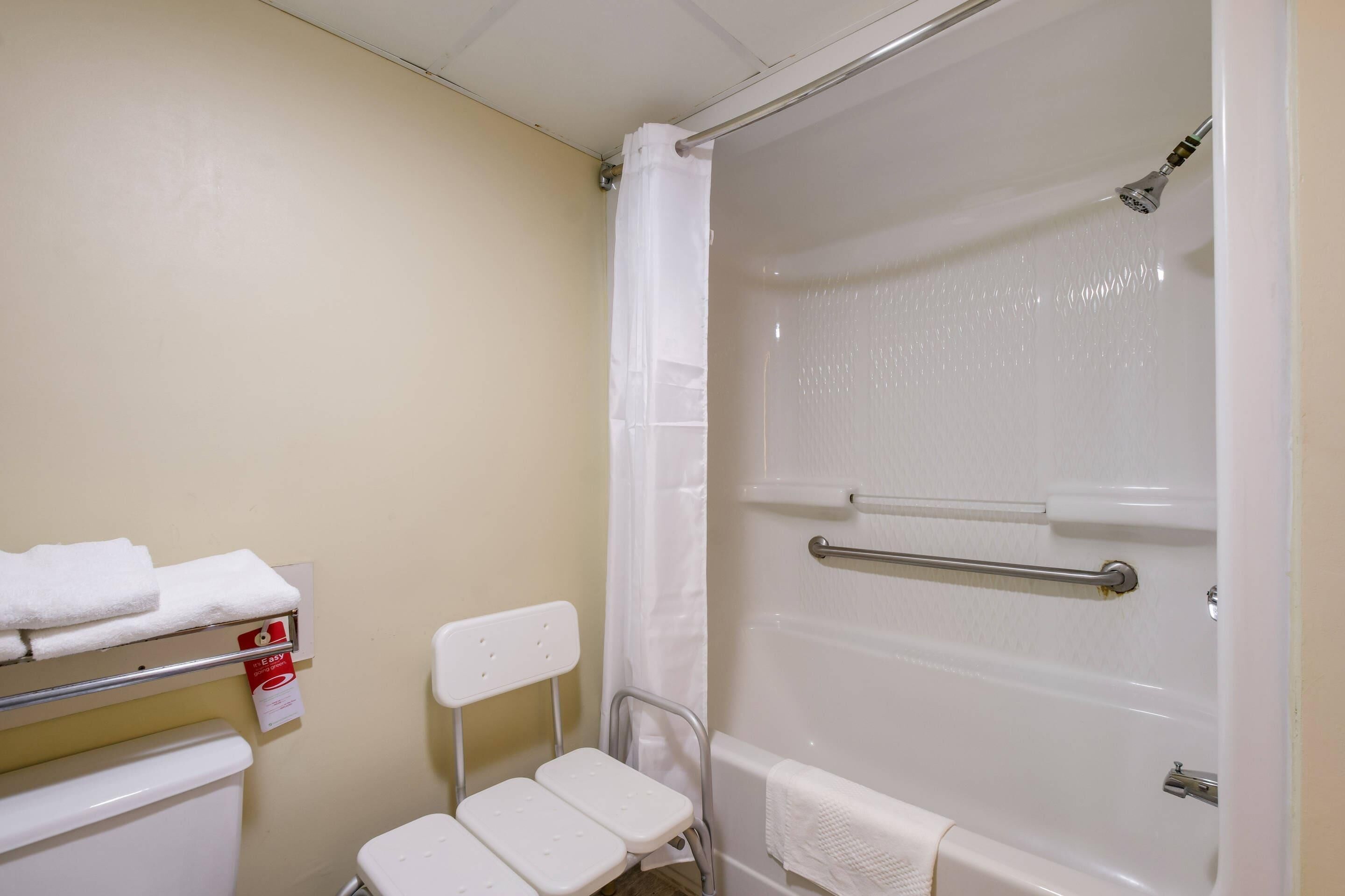 A bathroom with a shower, toilet, and a small white chair.