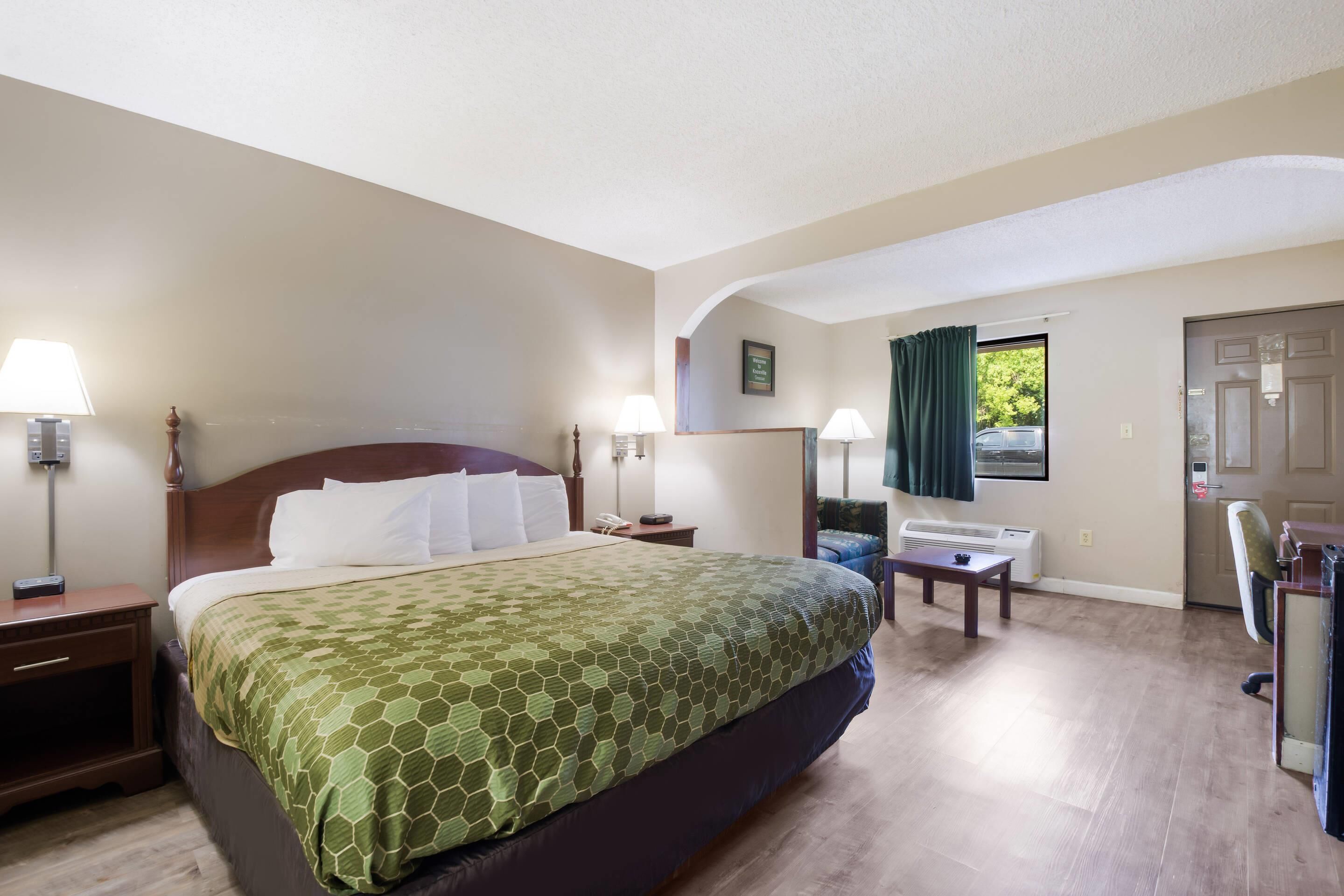 Une chambre d’hôtel avec un grand lit, deux tables de chevet avec des lampes, un bureau avec une chaise et une fenêtre avec des rideaux.