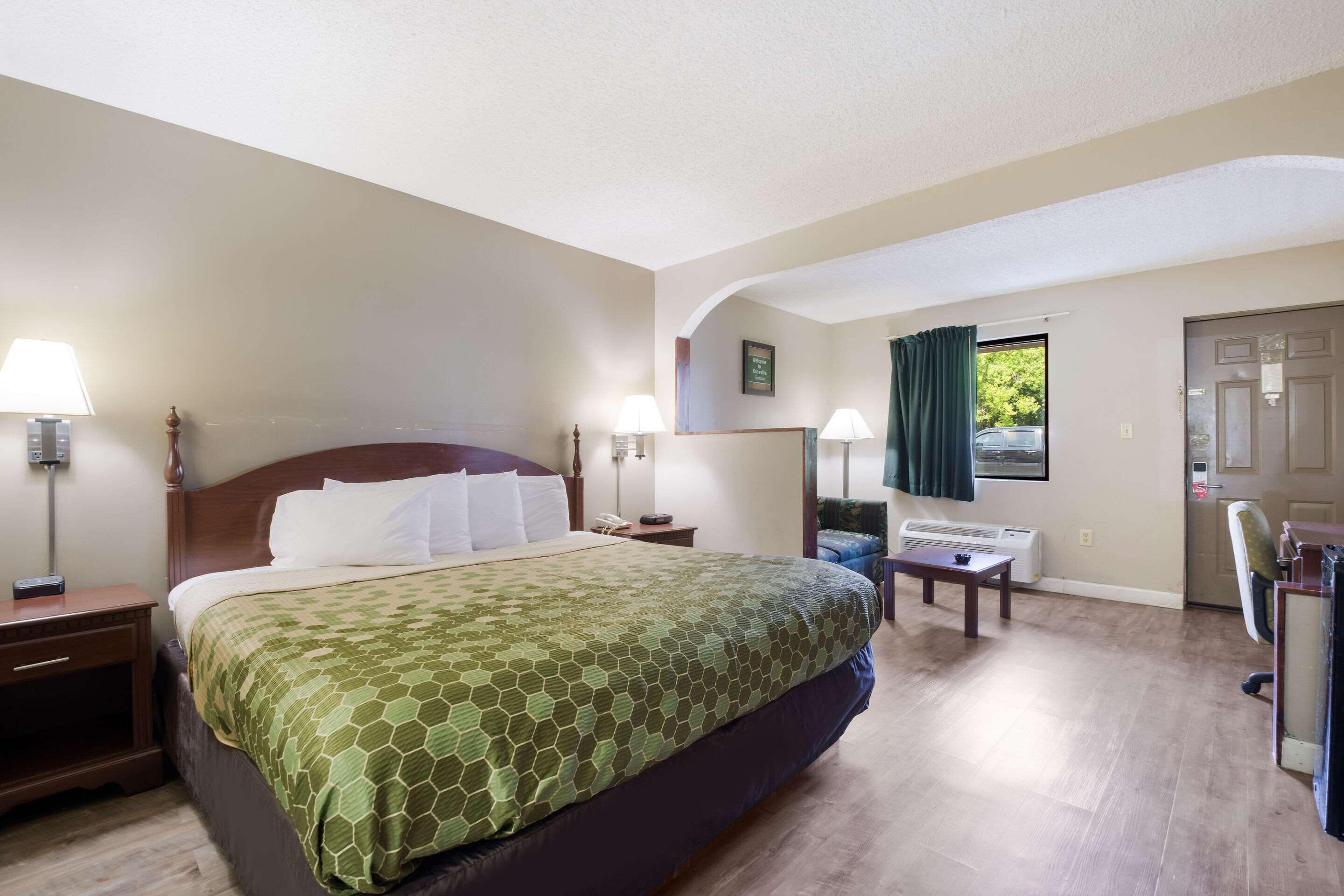 Une chambre d’hôtel avec un grand lit, des tables de chevet avec des lampes, un bureau avec une chaise et une fenêtre avec des rideaux.