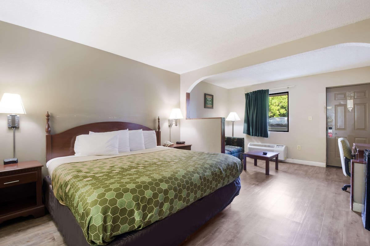 Une chambre d’hôtel avec un grand lit, des tables de chevet avec des lampes, un bureau avec une chaise et une fenêtre avec des rideaux.
