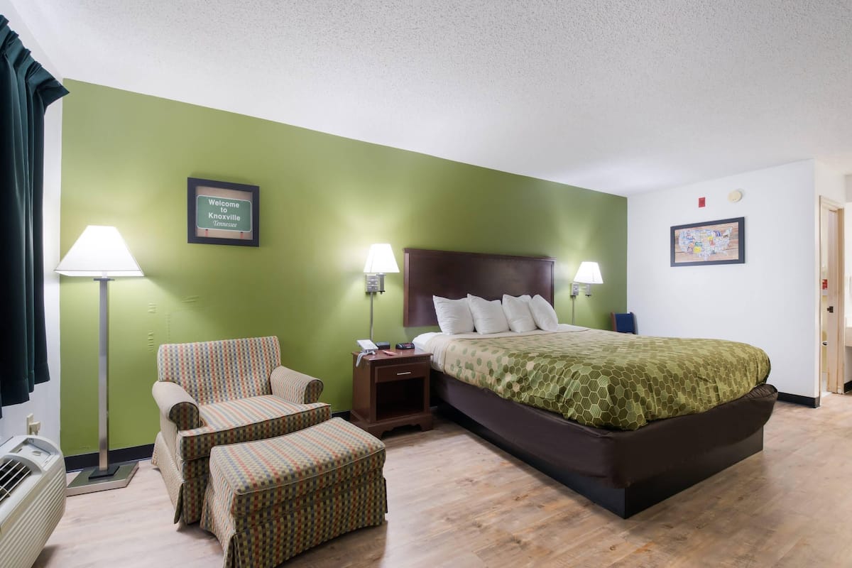 Une chambre d’hôtel avec un lit, deux chaises, une table de chevet et une lampe.