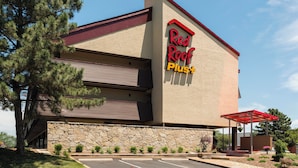 A Red Roof Plus hotel with a stone facade, a parking lot, and a red awning.
