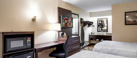 A hotel room with a desk, a television, a bed, a mirror, and a coffee maker.