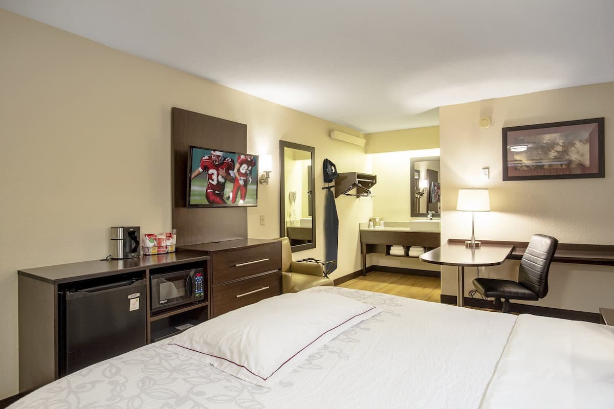 A hotel room with a bed, a desk, a chair, a microwave, a coffee maker, and a TV.