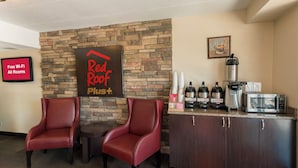 A Red Roof Plus hotel lobby with two leather chairs, a coffee station, and a sign indicating free Wi-Fi in all rooms.