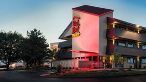 A Red Roof Plus hotel with a modern design, featuring a prominent red and white sign, a flat roof, and a well-lit entrance.