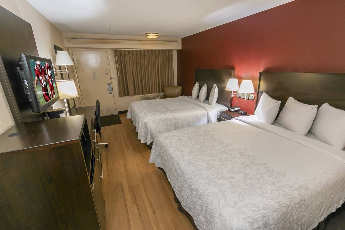 A hotel room with two beds, a desk with a television, and a window with curtains.