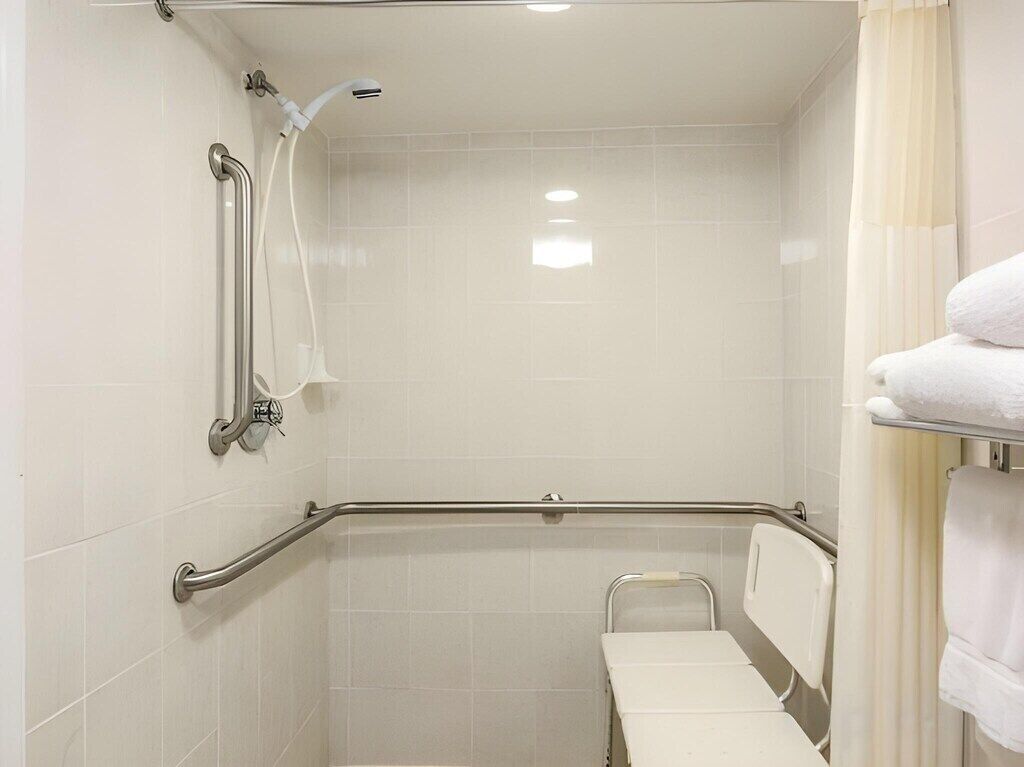 A bathroom with a shower, grab bars, a white bench, and a towel rack.