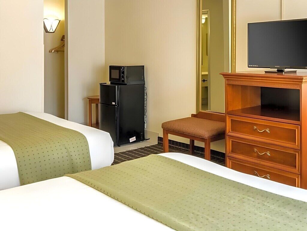 Une chambre d’hôtel avec deux lits, une télévision, un réfrigérateur, une commode en bois et un miroir.