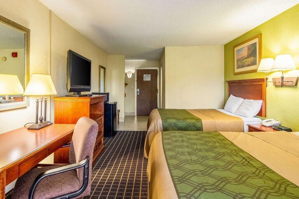 A hotel room with a desk, two beds, a television, and a mirror.
