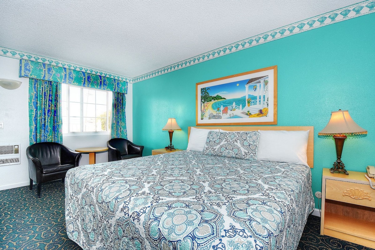 Ein Hotelzimmer mit Bett, zwei Sesseln, einem Schreibtisch und einem Bild an der Wand.