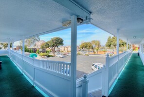 Un espacio al aire libre techado con alfombra verde, barandillas blancas y vistas a un estacionamiento y edificios.