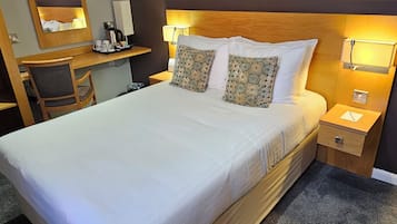 Una habitación de hotel con una cama grande, un escritorio, una silla, una mesita de noche y una lámpara de pared.