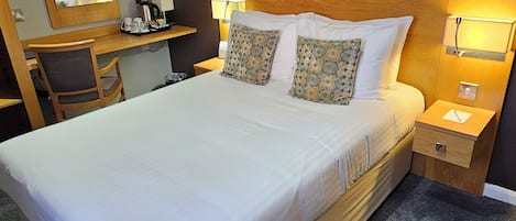 Una habitación de hotel con una cama grande, un escritorio, una silla, una mesita de noche y una lámpara de pared.