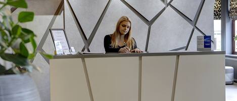 A reception desk with a geometric wall design, a potted plant, and a sign indicating a spa treatment.