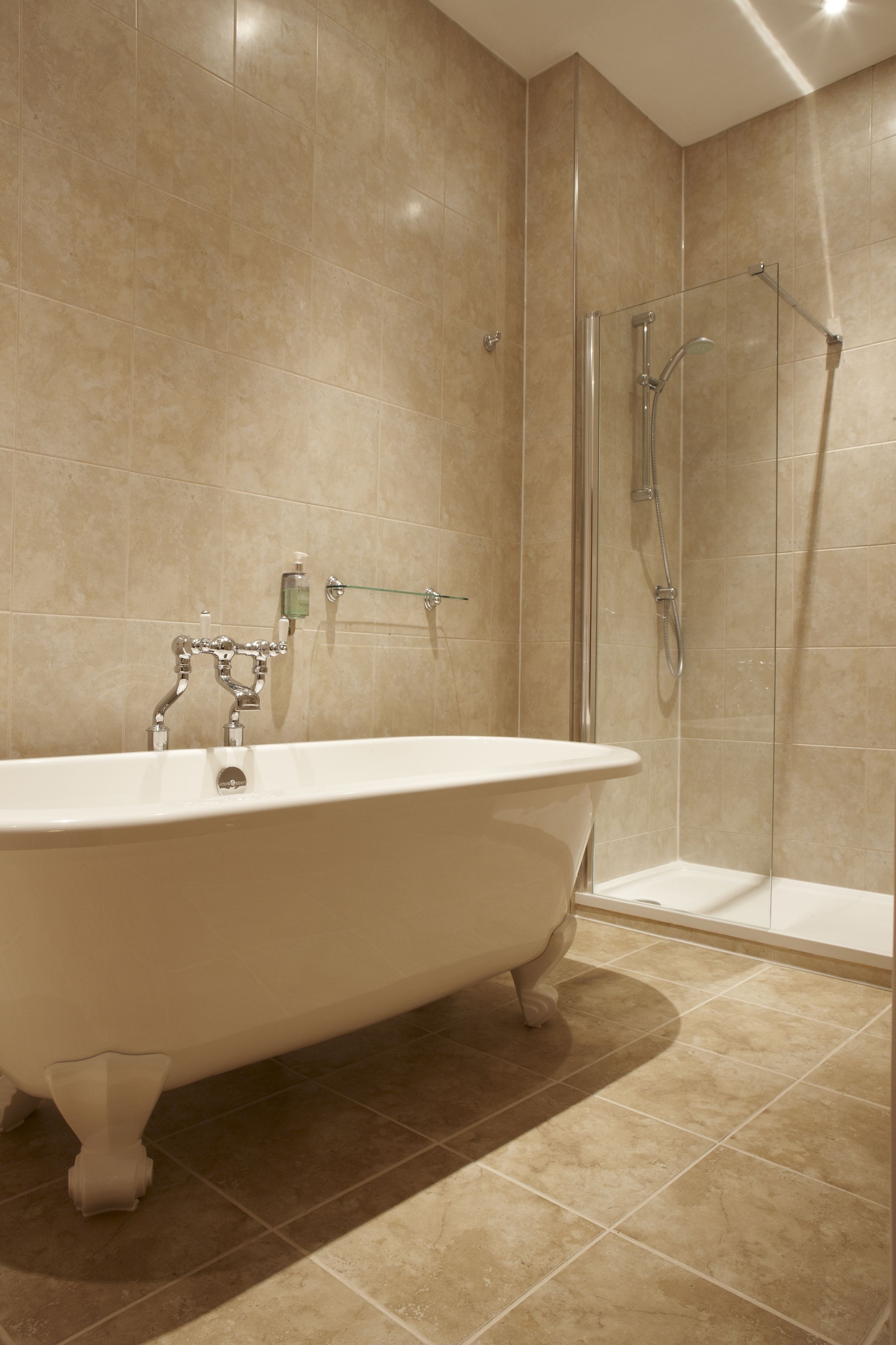 Un baño con bañera independiente, ducha con cerramiento de vidrio y paredes con azulejos color beige.
