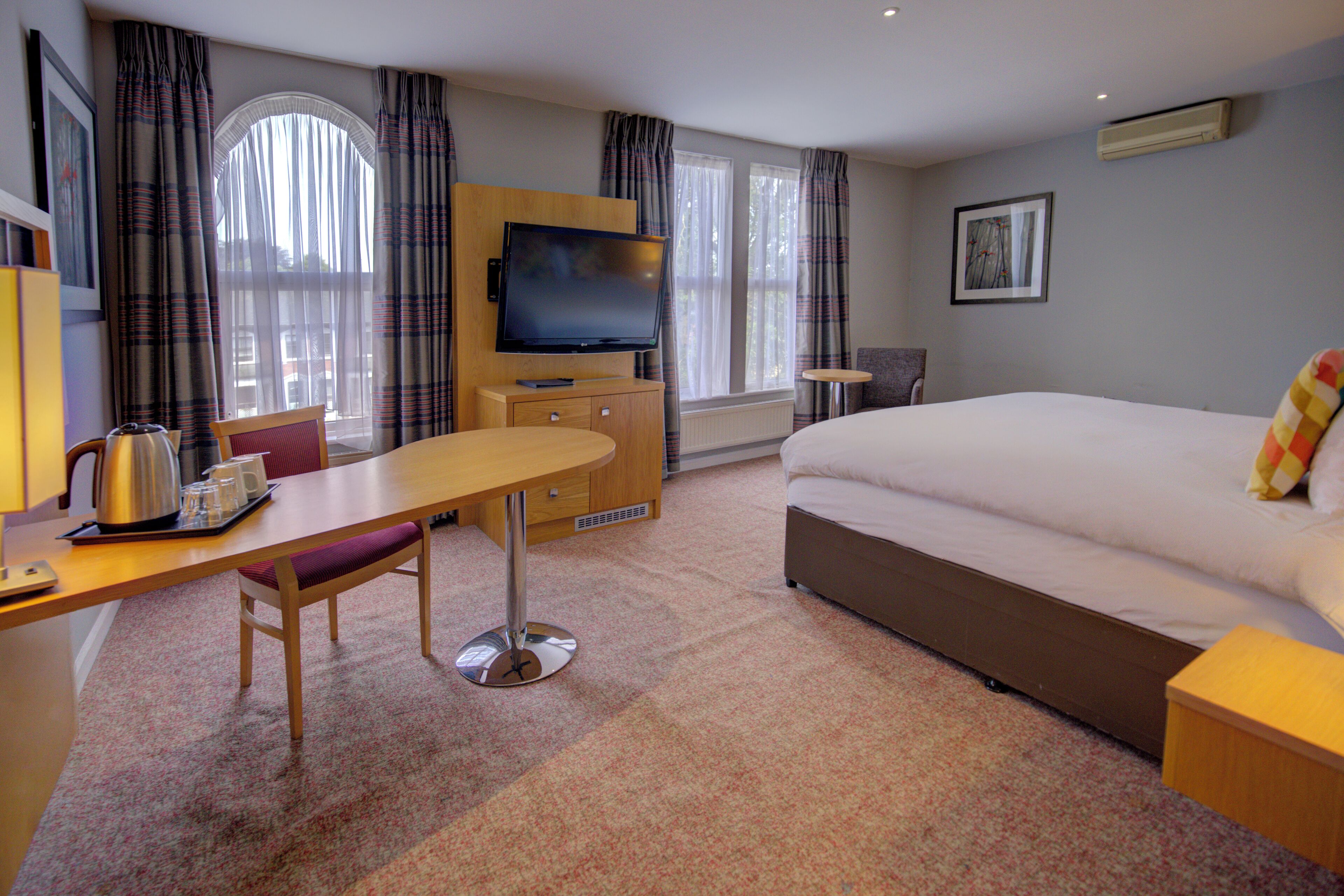A hotel room with a bed, a desk with a chair, a television, and a window with curtains.