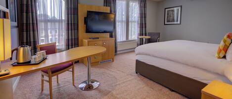A hotel room with a bed, a desk with a chair, a television, and a window with curtains.