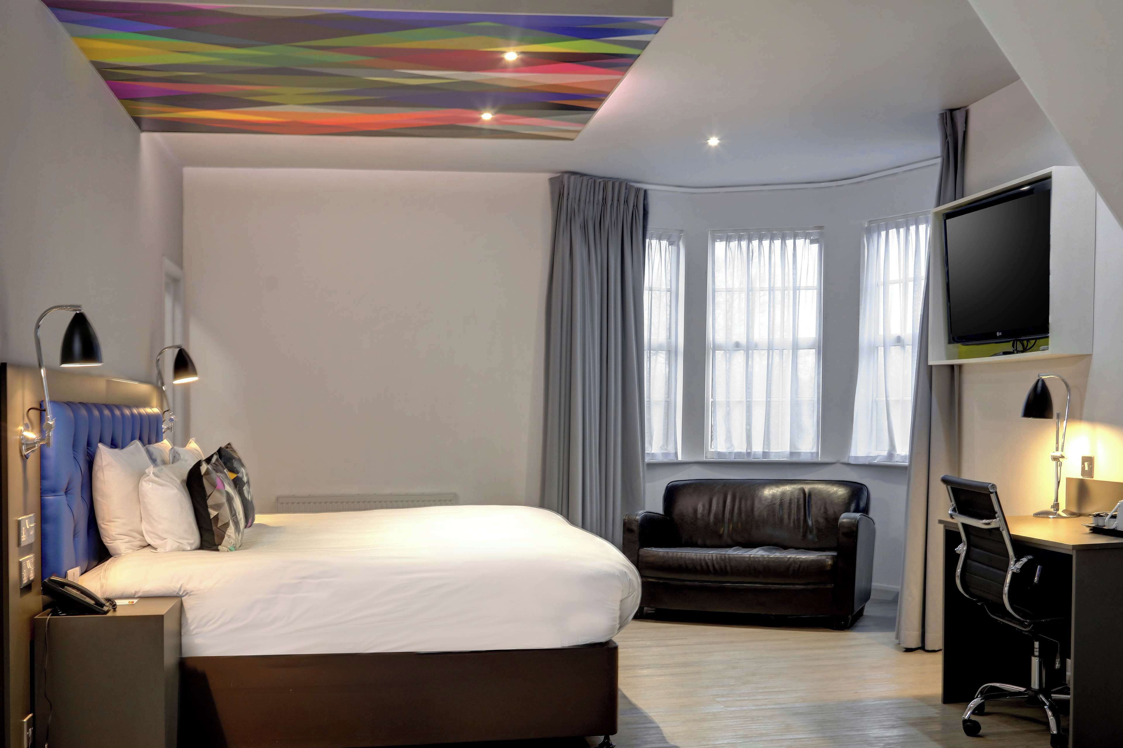 A modern hotel room with a large bed, a leather sofa, a desk with a computer, and a flat-screen TV.