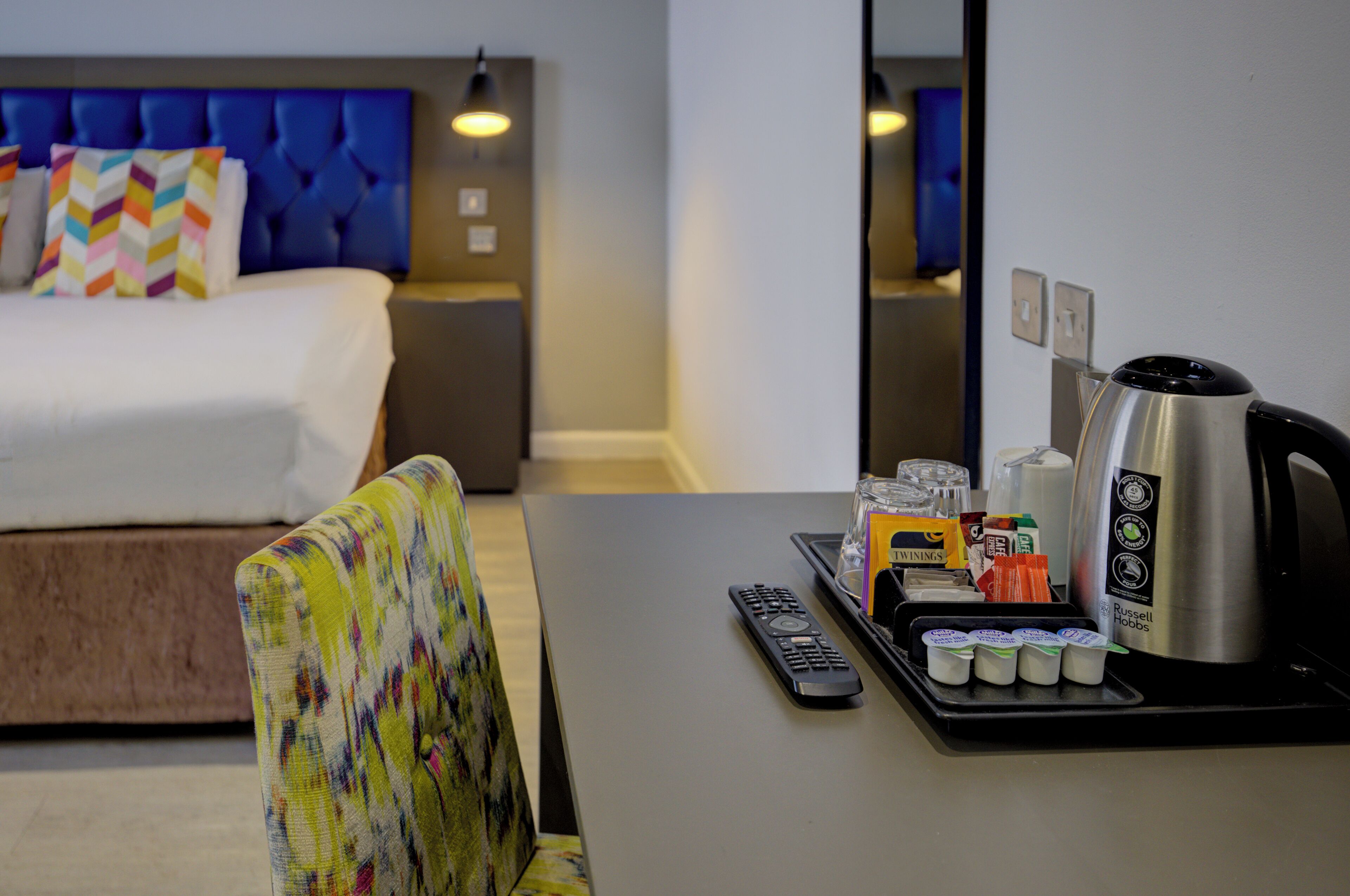 Een hotelkamer met een bed, een nachtkastje met waterkoker, bekers en een dienblad met diverse voorwerpen.