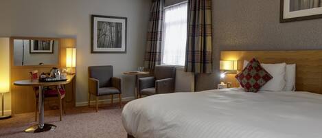 A hotel room with a large bed, a desk with a chair, a small table, and a window with curtains.