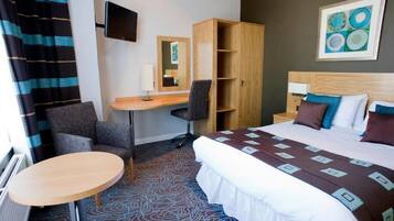 A hotel room with a bed, a desk, a chair, a small table, a wardrobe, and a TV on the wall.
