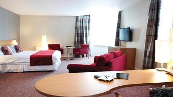 Una habitación de hotel con cama, escritorio, sofá rojo, televisión y lámpara.