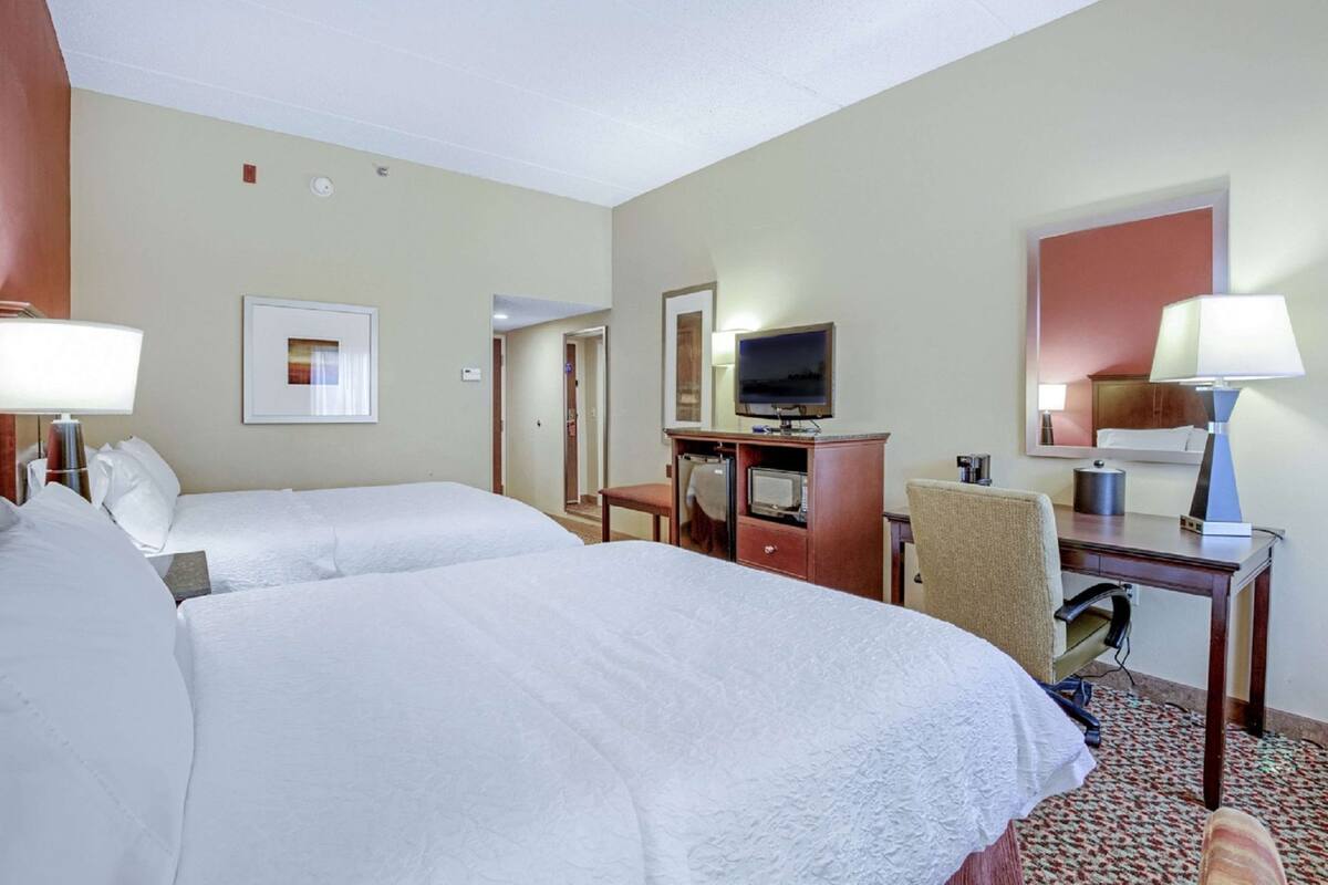 Une chambre d’hôtel avec deux lits, un bureau avec un ordinateur, une télévision et un miroir.