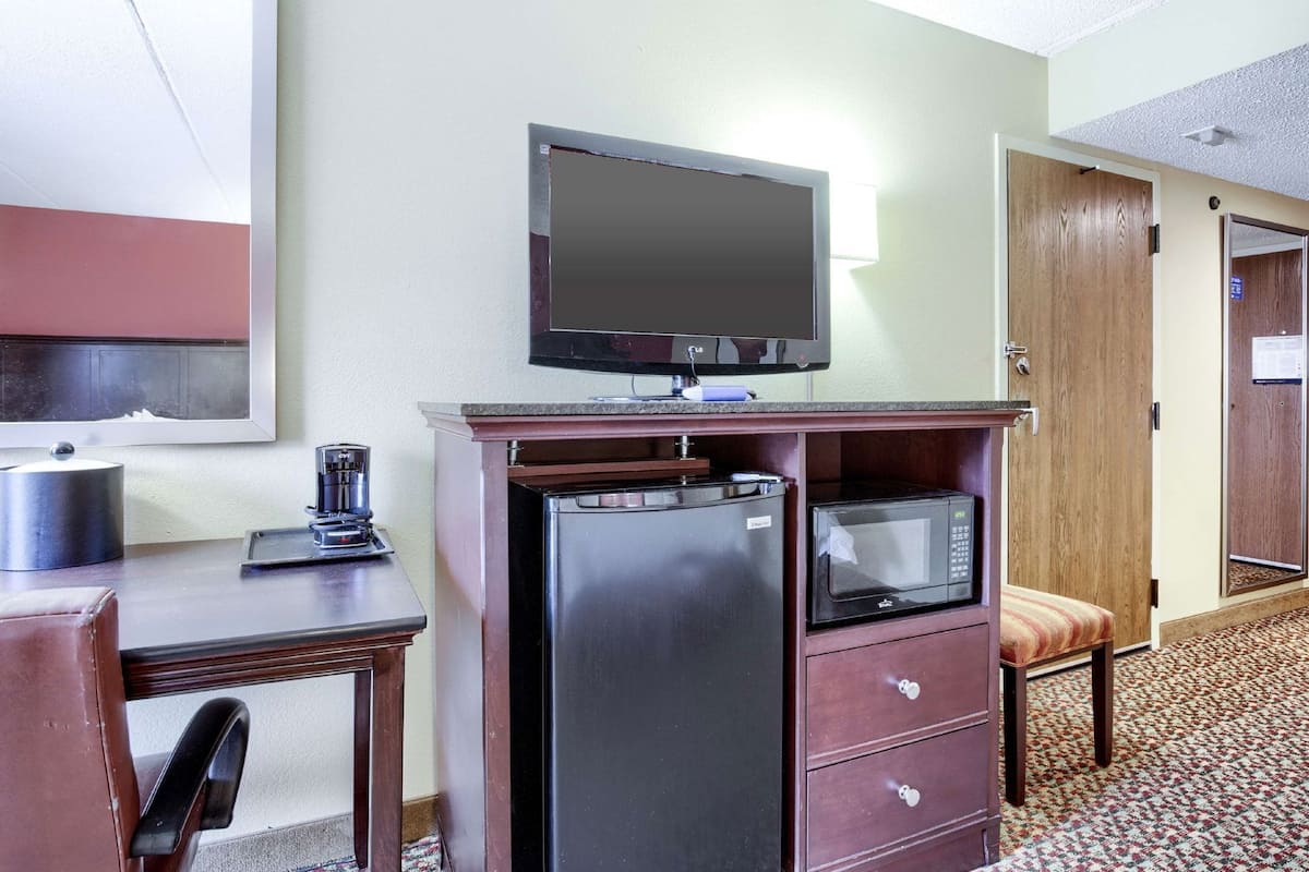 Une chambre d’hôtel compacte équipée d’une kitchenette, d’un téléviseur à écran plat, d’un four à micro-ondes, d’un réfrigérateur, d’une machine à café et d’un petit coin salon.