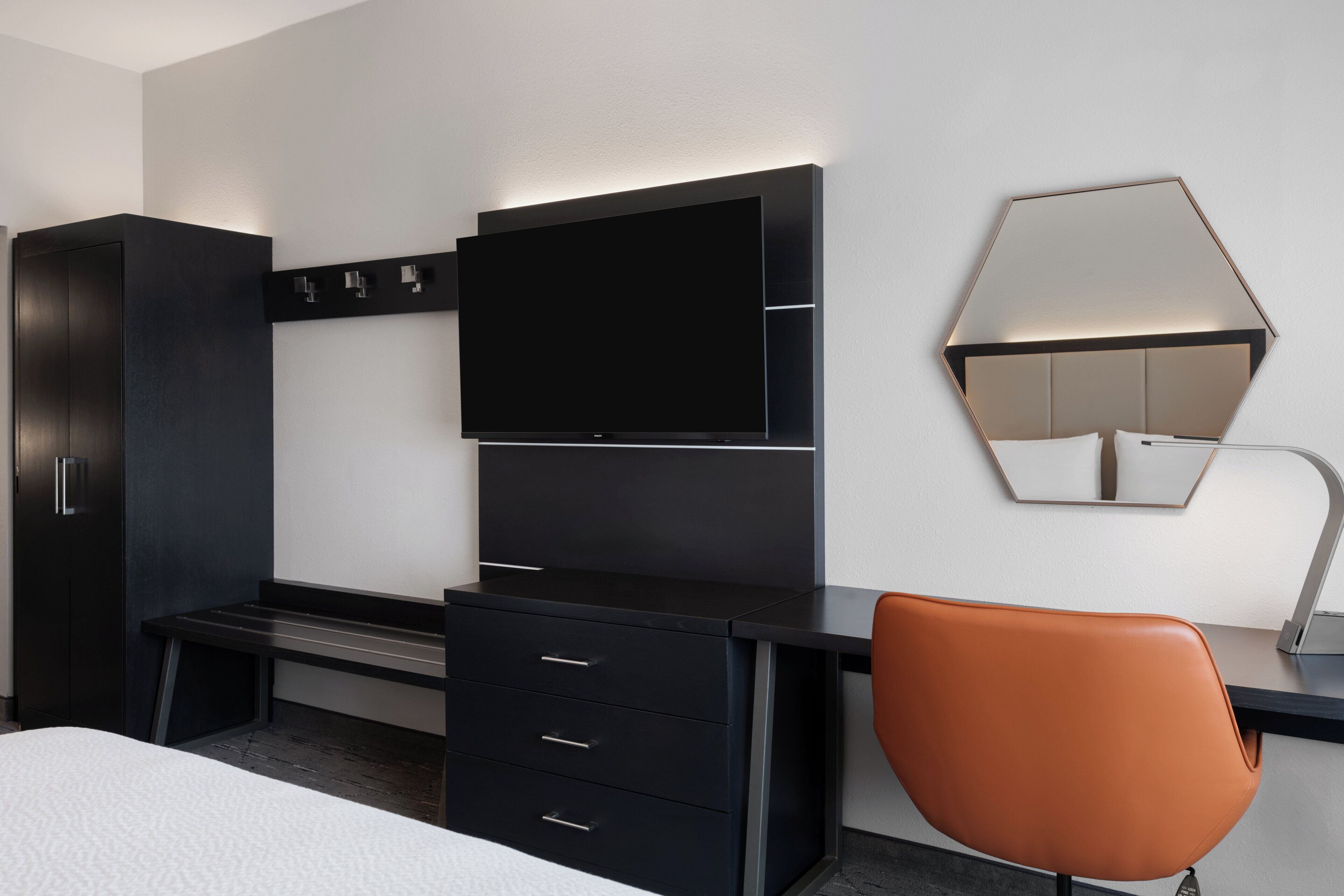 Een moderne hotelkamer met een zwart bureau, een flatscreen televisie, een grote spiegel en een bruine stoel.