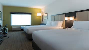 A hotel room with two beds, a desk, a chair, a window, and a wall-mounted lamp.