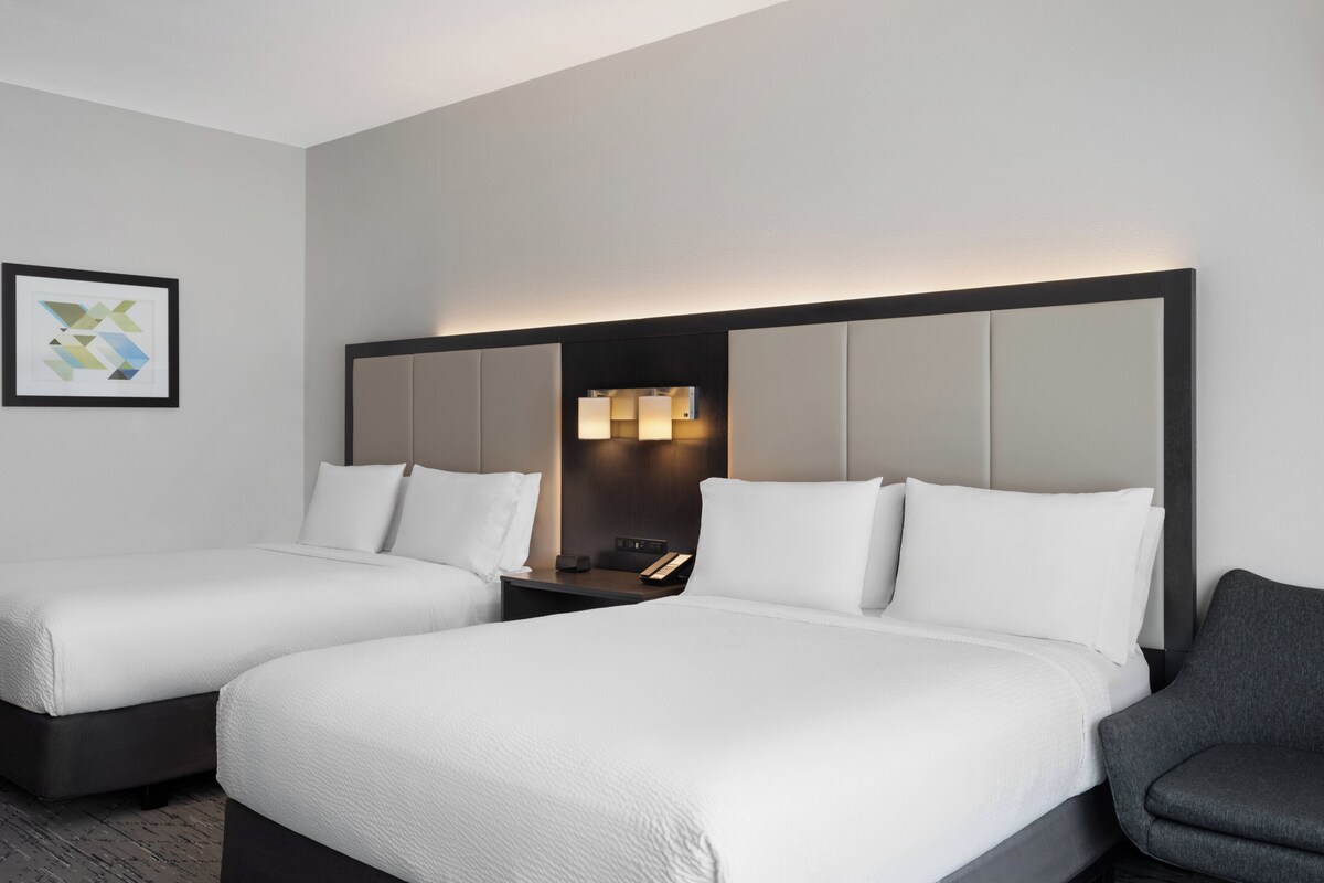 A hotel room with two beds, a nightstand, a lamp, and a framed picture on the wall.