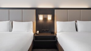Una habitación de hotel con dos camas, una mesita de noche con un teléfono y una lámpara, y una lámpara de pared.