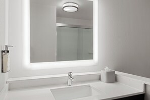 A modern bathroom with a white sink, a mirror with a light, and a glass shower enclosure. - Holiday Inn Express & Suites Tampa East - Ybor City by IHG (Tampa)