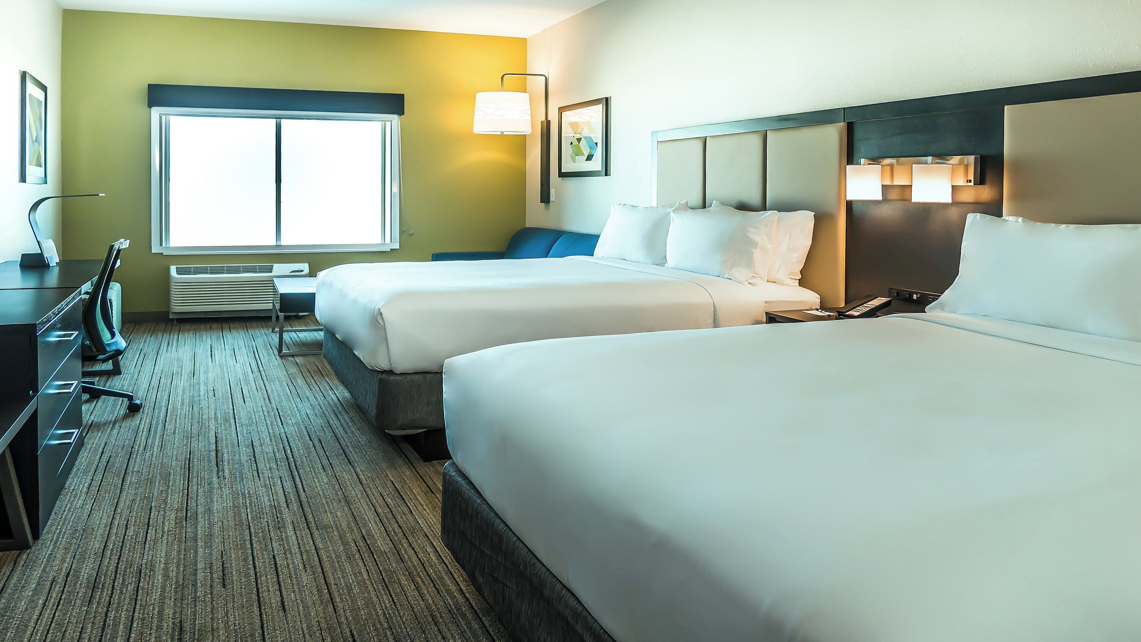 A hotel room with two beds, a desk, and a chair.